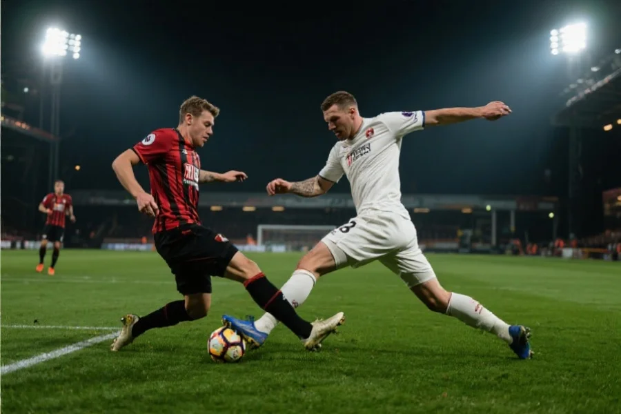 足球比赛中防守球员试图拦截对方前锋，场面紧张激烈，背景为灯光明亮的球场